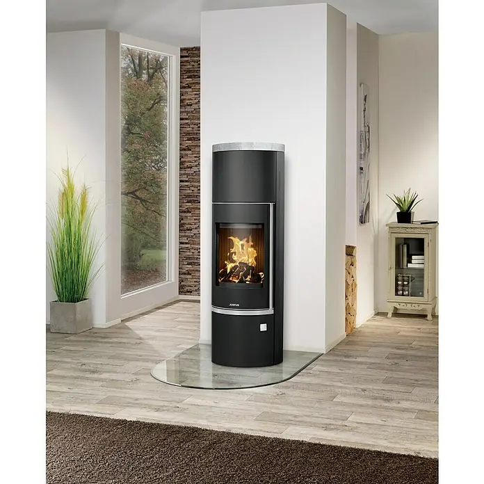 Justus Kaminofen Faro W+ 2.0 - 7 kW, Raumheizvermögen: 144 m³, Verkleidung: Stahl/Speckstein, Schwarz - Nahaufnahme eines eleganten Justus Kaminofens mit Glasbodenplatte, der Wärme und Stil in moderne Wohnräume bringt.