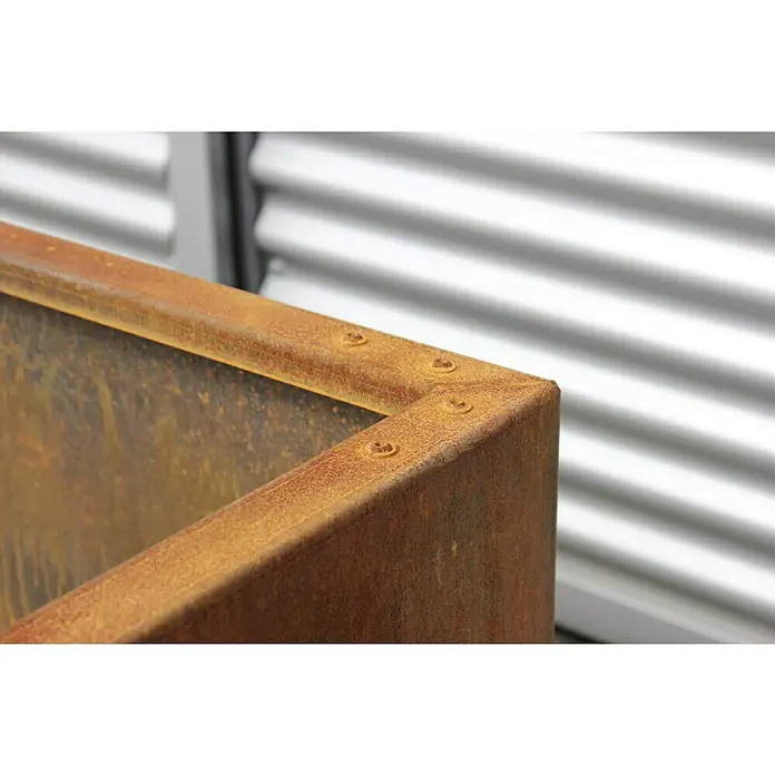 Palatino Hochbeet Urban L-Form - 200 x 200 x 70 cm, Stahl, Rostbraun - Nahaufnahme einer rostfarbenen Pflanzbox aus Cortenstahl, die mit Schrauben an den Ecken befestigt ist, vor einem Hintergrund aus Metallpaneelen.