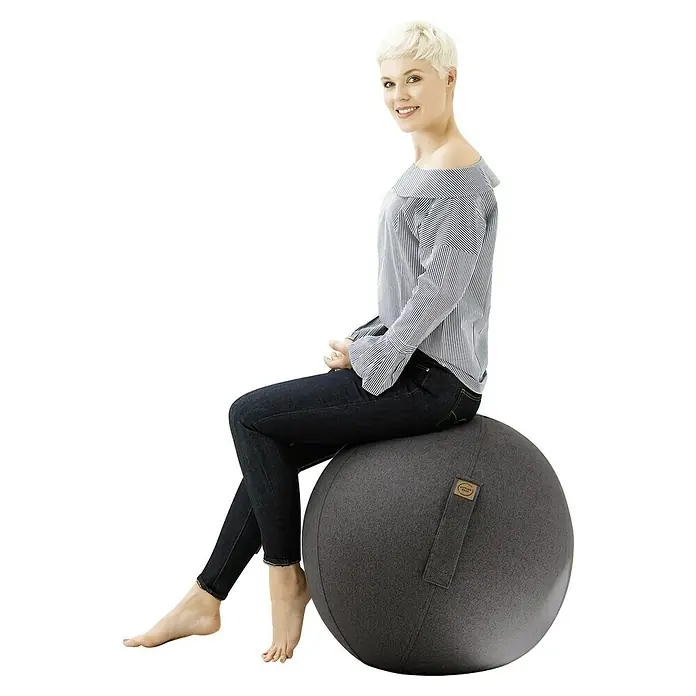 Sitting Ball Gymnastikball Felt - Anthrazit, Durchmesser: 65 cm, 100 % Polyester - Eine Frau sitzt auf einem grauen Sitzball. Der Sitzball ist mit einem Tragegriff versehen und die Frau trägt Jeans und eine gestreifte Bluse.