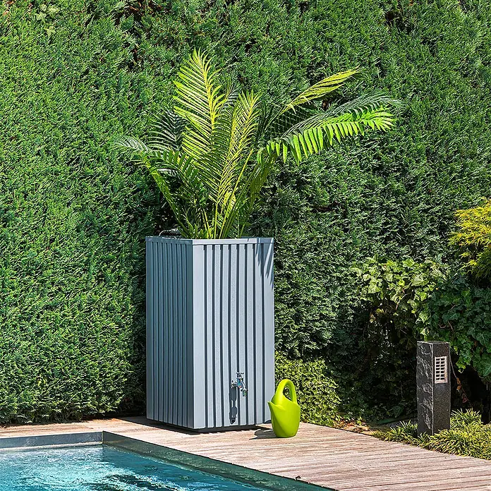 Roto Regentonne Balboa - L x B x H: 460 x 460 x 935 mm, Grau, Kunststoff - Ein grauer Regenspeicher mit vertikalen Streifen steht neben einem grünen Rasensprenger und Pflanzen, ideal zur Gartenbewässerung.