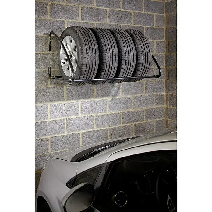 Mottez Metall-Reifen- & Lagerregal - L x B x H: 100 x 75 x 60 cm, Traglast: 100 kg - Reifenregal an einer Ziegelwand mit vier Reifen darauf, unter einem geparkten weißen Auto.