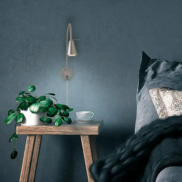 Briloner Foco de pared LED Comfort Light - Plata, 4 W - Elegante lámpara de pared de metal sobre una mesa de madera con una planta en maceta y una taza de café, junto a una cama acogedora.