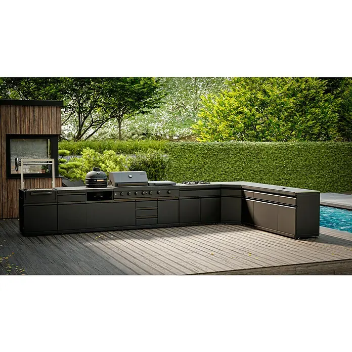 Kingstone Cube Outdoorküche I - 8 -tlg., Stahl, Sintered Stone, Schwarz, Material Grillfläche: Gusseisen, Anzahl Brenner: 11 Stk. - Outdoor-Küche mit Grill, Kochfeld und Spüle aus dunklem Material. Im Hintergrund befinden sich grüne Büsche und ein Pool.