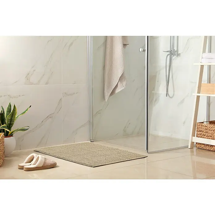 Badteppich Atlanta - 60 x 100 cm, Beige, 100% Baumwolle - Beige Badematte vor einer begehbaren Dusche, ergänzt durch Hausschuhe und Zimmerpflanze, schafft eine entspannende Badezimmeratmosphäre.