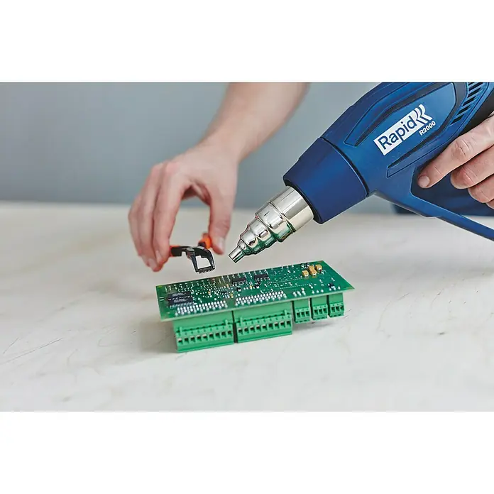 Rapid Pistola de aire caliente R2000 - 2.000 W, Rango de temperaturas: 60 °C - 600 °C - Se está utilizando una pistola de aire caliente Rapid R2000 para reparar un componente en una placa de circuito verde.