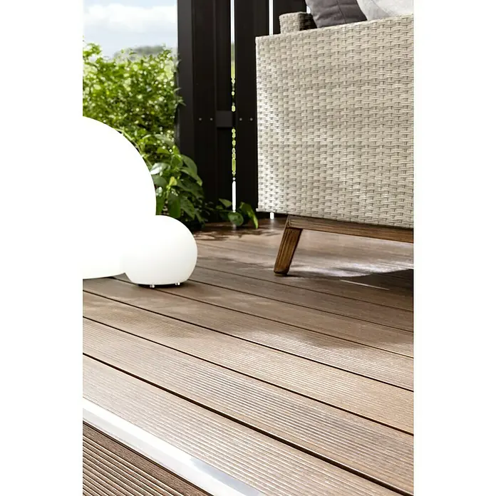 b!design WPC-Terrassendiele Ipe - 300 x 13,8 x 2,25 cm, Ipe - Nahaufnahme eines Teils einer Terrasse mit Holzboden, einem weißen kugelförmigen Licht und einem Outdoor-Sessel mit hellen Bezügen.