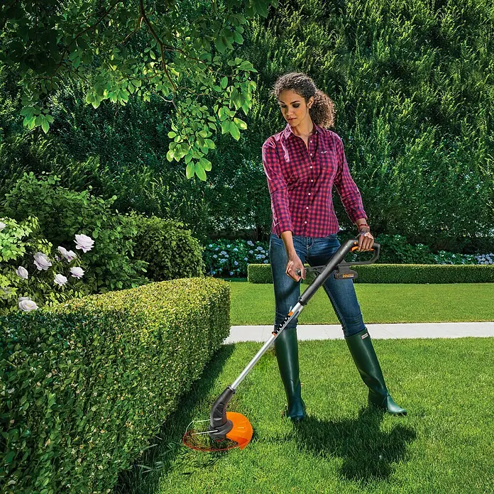 Worx PowerShare 20V Akku-Rasentrimmer WG157E.9 - 20 V, Li-Ionen, Ohne Akku - Frau trimmt Hecke mit WORX Akku-Rasentrimmer mit Kantenschneider für präzise Ergebnisse und mühelose Gartenarbeit.