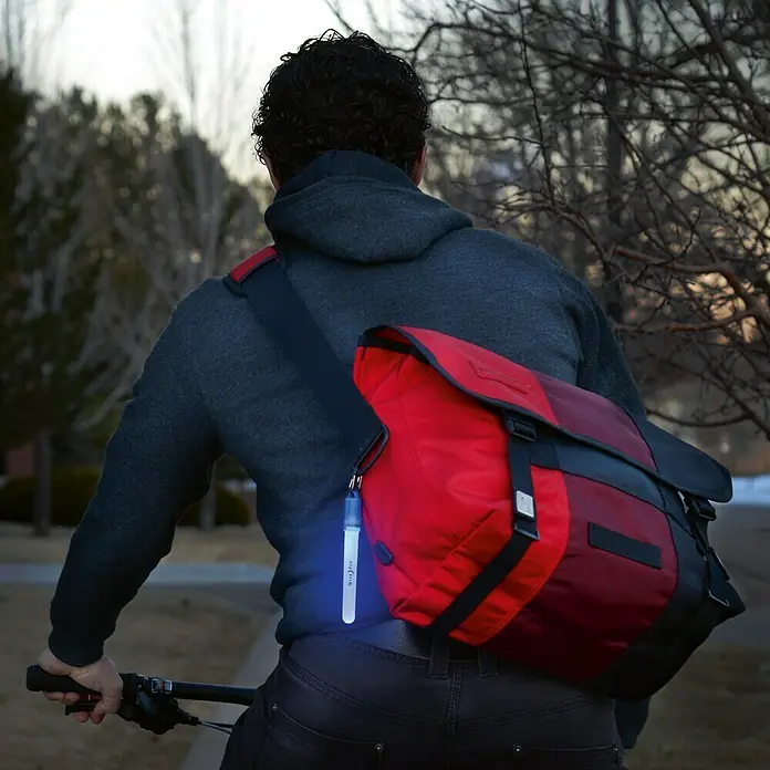 Nite Ize Barra luminosa LED mini - Azul - Un hombre anda en bicicleta con una bolsa roja y una barra luminosa Nite Ize brillante para mayor visibilidad.