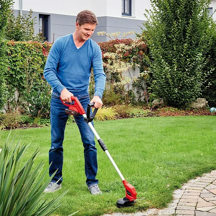 Einhell Power X-Change 18V Akku-Rasentrimmer GC-CT 18/24 Li-Solo - 18 V, Li-Ionen, Ohne Akku - Ein Mann benutzt einen roten Rasentrimmer, um den Rasen in seinem Garten zu schneiden. Das Gerät ist benutzerfreundlich und effizient.