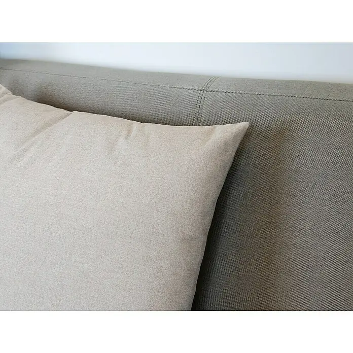 Kissen Ned - Sand, 45 x 45 cm, 100 % Polyester - Nahaufnahme eines hellbeigen Kissens vor einem grauen gepolsterten Kopfteil, das Komfort und Stil im Schlafzimmer betont.
