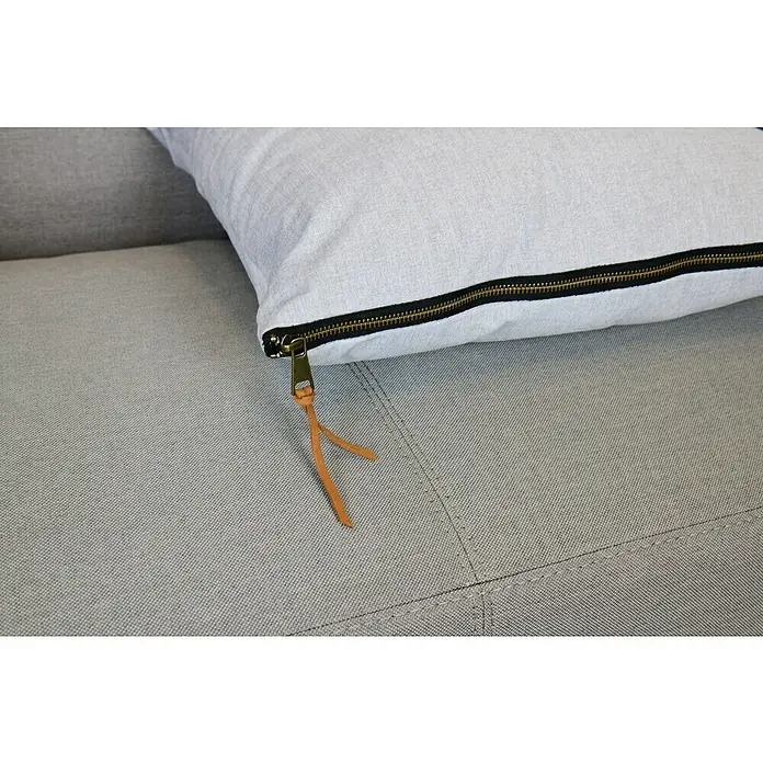 Kissen Ned - Grau, 45 x 45 cm, 100 % Polyester - Detailaufnahme eines hellgrauen Kissens mit Reißverschluss und Lederband auf einem grauen Sofa.
