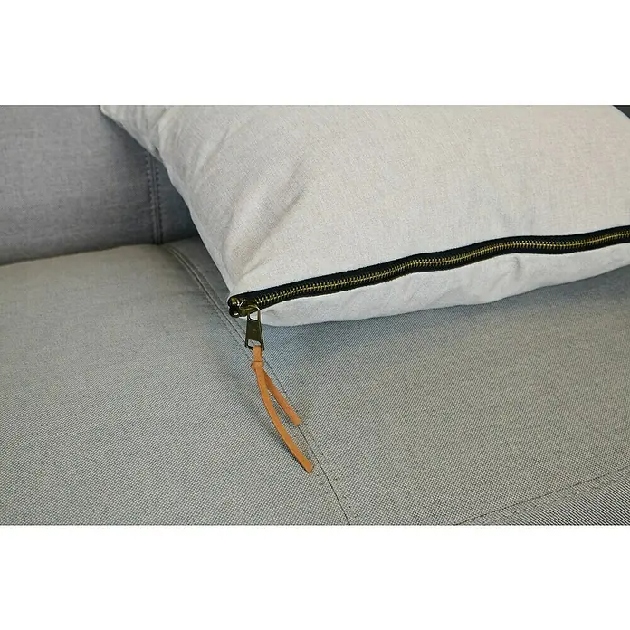 Kissen Ned - Sand, 45 x 45 cm, 100 % Polyester - Nahaufnahme eines hellgrauen Sofakissens mit Reißverschluss und Lederband auf einem grauen Sofa.