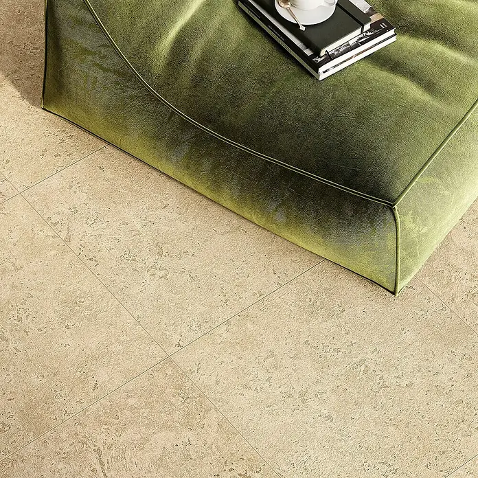 Corso Italia Terrassenfliese Pompei Aureo Crosscut - 60 x 60 cm, Beige, Matt - Ein grüner Sitzhocker steht auf einem Boden mit beigen Fliesen. Auf dem Hocker liegen Bücher und eine Tasse.