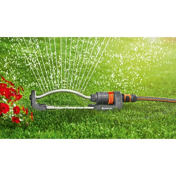 Gardena Aspersor oscilante Aqua S - Superficie de rociador máx.: 220 m² - Aspersor oscilante de Gardena en acción, regando un césped verde con flores rojas, asegura un riego uniforme y eficiente.