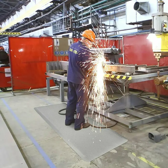 Floordirekt Bodenschutzmatte Heavy-Duty Soft - 90 x 305 cm, Grau - Arbeiter mit Sicherheitsausrüstung steht auf einer grauen Anti-Ermüdungsmatte.