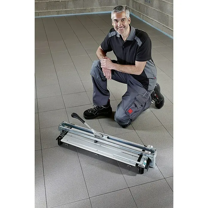 Wolfcraft Cortador manual de azulejos TC 710 PM - Longitud de corte máx.: 710 mm, Espesor máx. de azulejo: 14 mm - Hombre arrodillado junto a un cortador de azulejos sobre un suelo embaldosado. La herramienta es un cortador manual, ideal para cortes precisos.