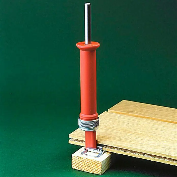 Staba Clavadora eléctrica - Plástico - La imagen muestra una herramienta de instalación de pisos laminados con mango rojo y detalles plateados, utilizada en pisos de madera.