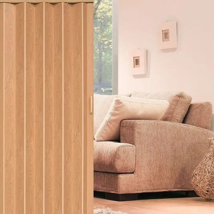 Falttür - PVC, Eiche, 100 x 200 cm - Eine helle Holztür mit Lamellen steht neben einem beigen Cordsofa, das mit Kissen und Bildern an der Wand gemütlich wirkt.