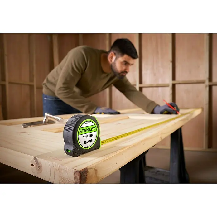 Stanley Cinta métrica extensible Hi-Vis - Largo: 5 m - Un artesano usa una cinta métrica Stanley Tylon para realizar mediciones precisas en un marco de madera.
