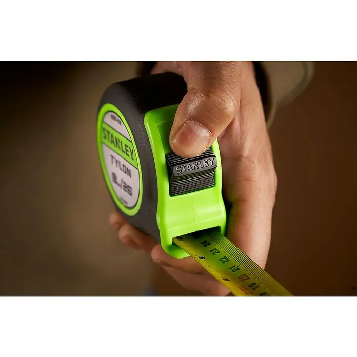 Stanley Cinta métrica extensible Hi-Vis - Largo: 8 m - Primer plano de una cinta métrica Stanley sostenida en una mano, mostrando una escala de medición amarilla con marcas negras.