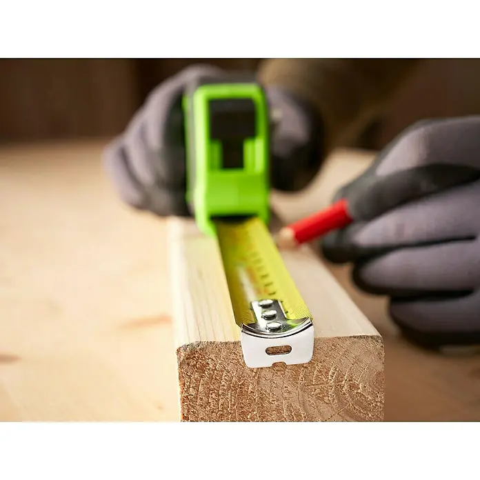Stanley Cinta métrica extensible Hi-Vis - Largo: 8 m - Primer plano de una cinta métrica amarilla sobre un tablón de madera, marcada con un lápiz rojo por manos enguantadas.