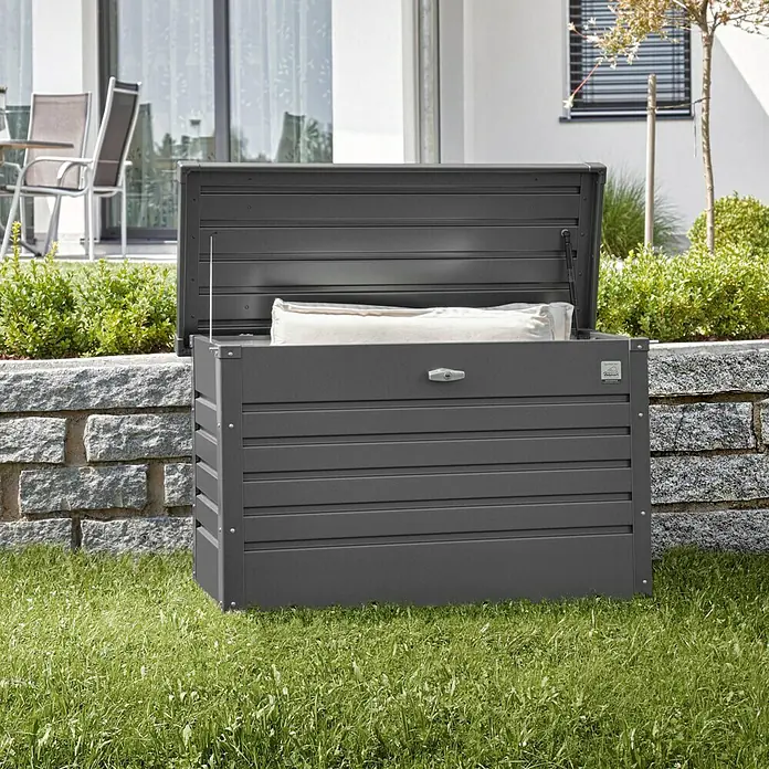 Biohort FreizeitBox Gartenbox FreizeitBox 100 - L x B x H: 101 x 46 x 61 cm, Dunkelgrau Metallic, Stahl - Hier ist eine graue Gartenbox mit offenem Deckel. Sie steht auf einer grünen Rasenfläche vor einer Steinmauer.