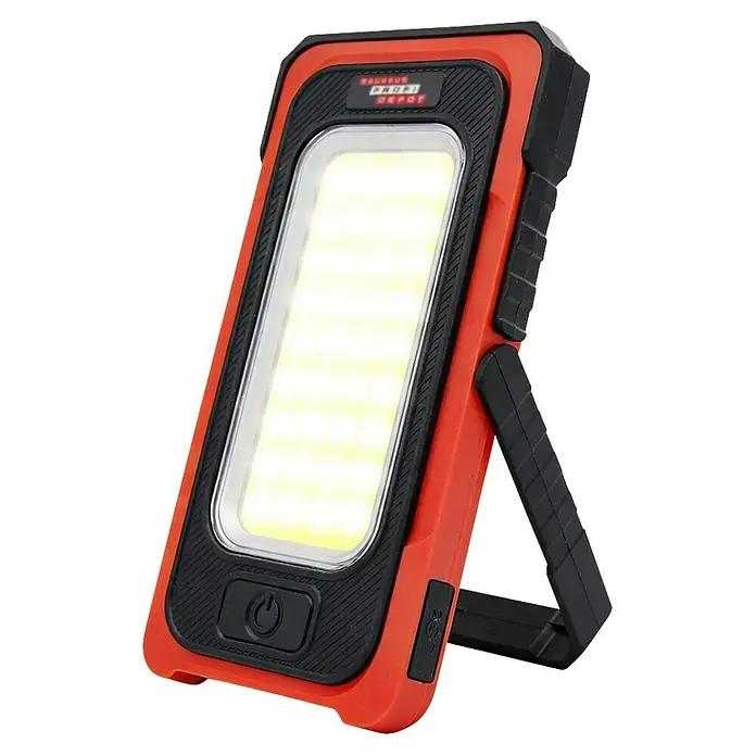 Profi Depot Linterna - Con energía solar, 750 lm, Con imán - Una luz de trabajo roja BAUHAUS PROFI DEPOT con adornos negros, un panel LED y un pie para una iluminación versátil en talleres y garajes.