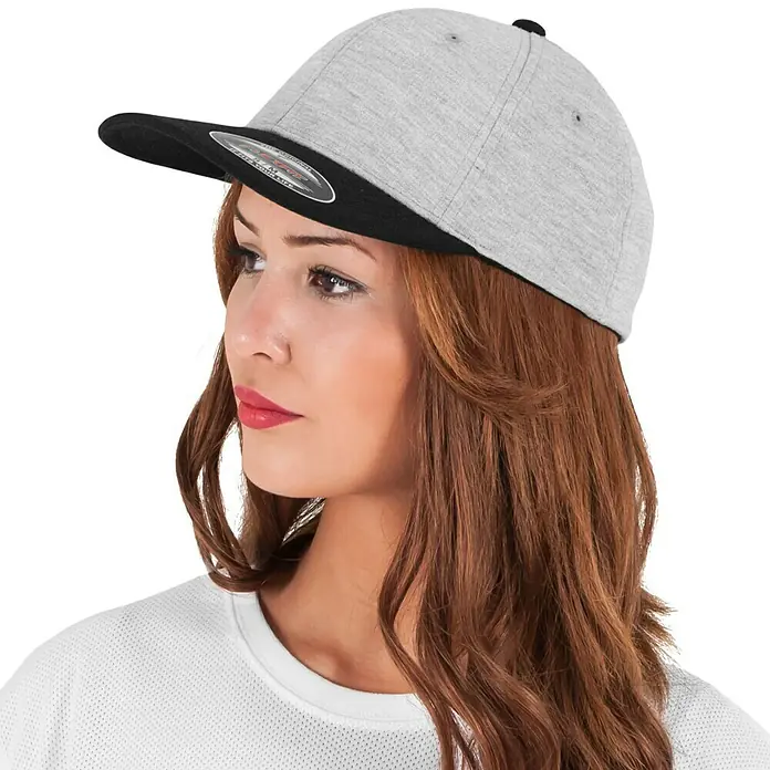 Flexfit Gorra Double Jersey - Gris/Negro, S/M - Gorra Flexfit gris con visera negra, usada por una mujer mirando de lado. El accesorio perfecto para un look casual.