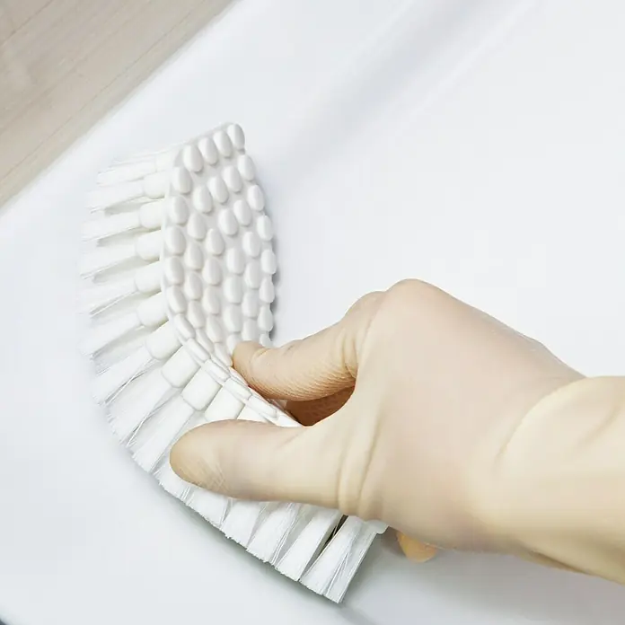 Haug Flexobürste - Material Borsten: Kunsthaar, 19 x 7 x 4 cm, Kunststoff - Detailaufnahme einer Hand mit Einweghandschuh, die eine weiße Bürste auf einer weißen Oberfläche hält.