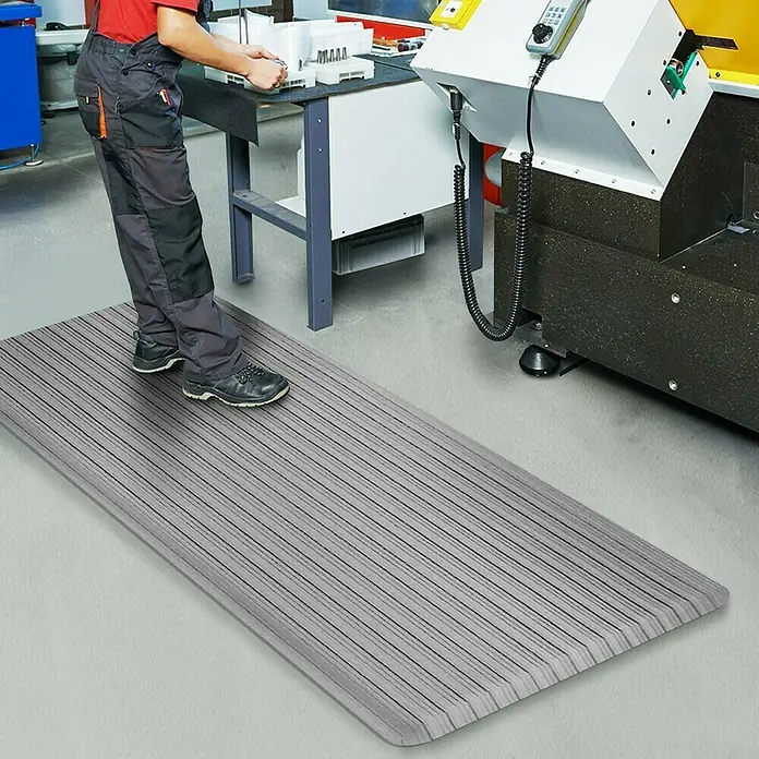 Floordirekt Bodenschutzmatte Heavy-Duty Ripp - 90 x 305 cm, Grau - Eine graue, gestreifte Arbeitsplatzmatte für Komfort und Sicherheit am Steharbeitsplatz in einer Werkstatt.