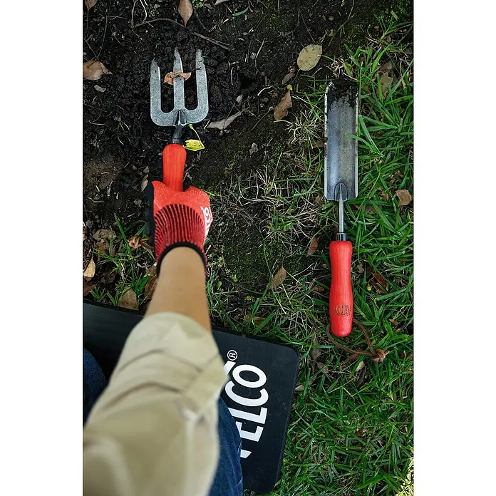 Felco Handgabel 431 - 33 cm - Gartengeräte wie eine kleine Harke und ein Pflanzholz liegen auf dem Rasen neben einer Person, die eine Kniematte benutzt.