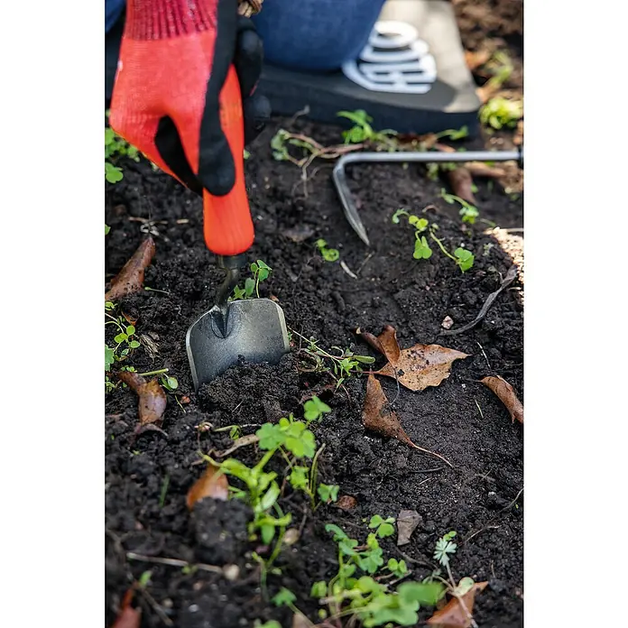 Felco Blumenkelle 401 - 33 cm - Nahaufnahme einer orangefarbenen Gartenhandschuhhand, die einen silbernen Spaten in dunkle Gartenerde drückt, mit Unkrautjätern und Kniekissen im Hintergrund.