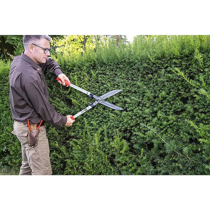 Felco Hand-Heckenschere 250-63 - L x B x H: 71 x 25 x 11 cm, Rot - Ein Mann schneidet eine grüne Hecke mit einer silbernen Gartenschere mit roten Griffen. Der Mann trägt eine braune Hose und ein braunes Hemd.