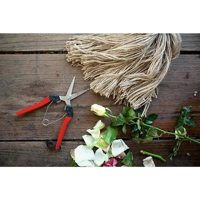 Felco Ernteschere 322 - Bypass, Max. Aststärke: 10 mm - Rosenschnitt mit einer Gartenschere auf einem rustikalen Holztisch, ergänzt durch eine Rolle Bindfaden und abgefallene Blütenblätter.