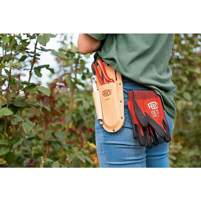 Felco Holster 910+ - Passend für: Felco Baum-, Reb-, Gartenscheren und Schleifstein 903 - Nahaufnahme von Gartengeräten, darunter eine Felco-Schere, Handschuhe und ein Holster, die an einer Jeans befestigt sind.