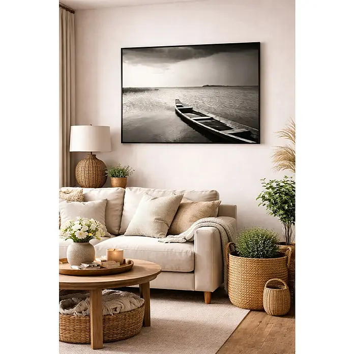 Lienzo Barca B&N - Barca B&N, An x Al: 50 x 70 cm - Salón con sofá color crema, mesa de madera, detalles de cestería y una foto en blanco y negro enmarcada de un barco en la pared.