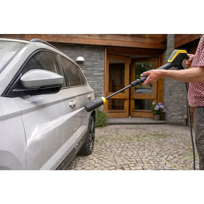 Kärcher Hochdruckreiniger K 7 Comfort Premium Connect Home - 3.000 W, Max. Druck: 180 bar, Fördermenge: 600 l/h, Inkl. Home-Kit - Ein Mann reinigt mit einem Hochdruckreiniger ein graues Auto vor einem Haus, wobei der Fokus auf dem Kärcher Gerät liegt.