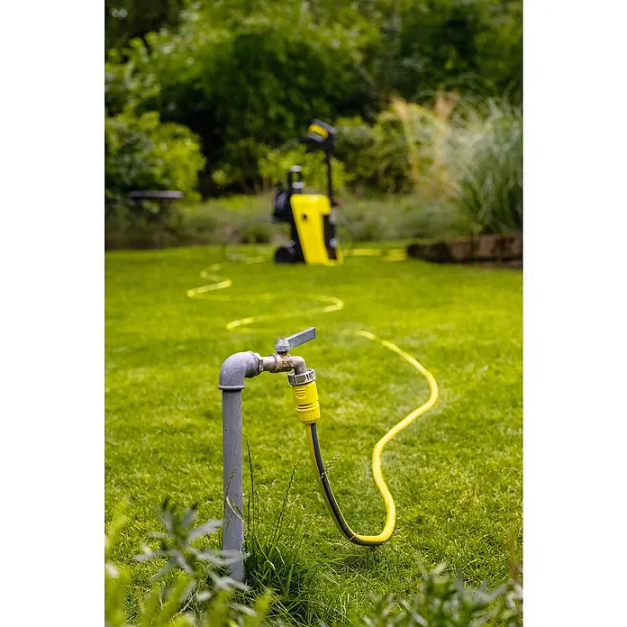 Kärcher Hochdruckreiniger K 5 Comfort Premium - 145 bar, 2.100 W, Fördermenge: 500 l/h, Ohne Home-Kit - Außenhahn mit gelbem Schlauchanschluss auf einem Rasen. Im Hintergrund ist ein gelber Hochdruckreiniger zu sehen, bereit für die Gartenarbeit.