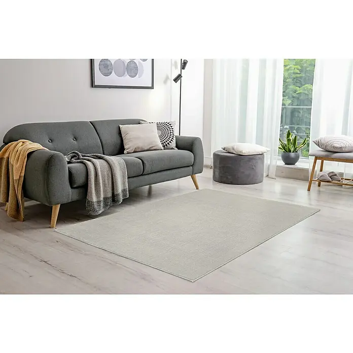 Alfombra de pelo largo Lauria - Crema, 230 x 160 cm, 100% Poliéster - Una alfombra gris claro está colocada en la sala de estar con un sofá gris, un taburete y una ventana para un ambiente acogedor.