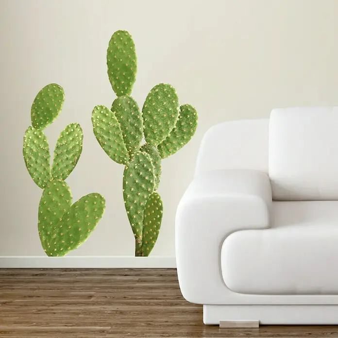 Vinilo de pared El Paso - 48 x 68 cm, Plástico - Un primer plano de dos plantas de chumbera frente a una pared blanca, junto a un elegante sofá blanco en la habitación.
