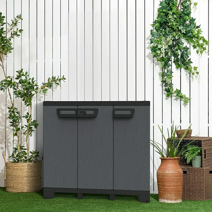 Terry Kunststoff-Mehrzweckschrank CAB 102B ARDESIA - H x B x T: 93,5 x 102 x 39 cm, Schwarz - Grauer Kunststoff-Gartenschrank mit drei Türen vor weißem Lattenzaun, dekoriert mit Pflanzen. Praktische Aufbewahrung für den Außenbereich.