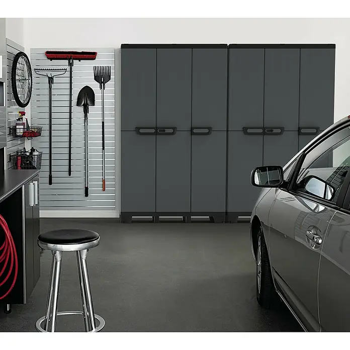 Terry Kunststoff-Mehrzweckschrank CAB 102A ARDESIA - H x B x T: 172 x 102 x 39 cm, Schwarz - Eine Garage mit grauen Schränken und Werkzeugen an der Wand. Ein Hocker steht davor und ein Auto ist zur Hälfte sichtbar.