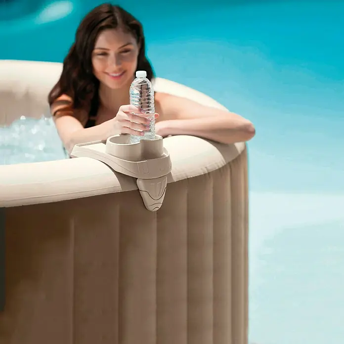 Intex Soporte para bebidas - Específico para: Spa - Primer plano de una bañera de hidromasaje con una mujer al fondo y un portabebidas con una botella de agua en primer plano.