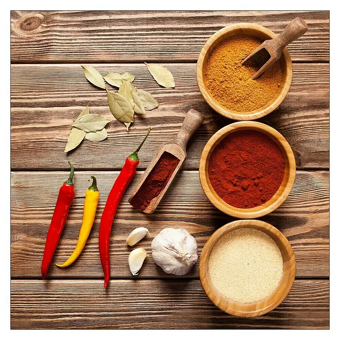 ProArt Kitchen Glasbild - Herbage In Bowl III, B x H: 30 x 30 cm - Holzschalen mit Gewürzen, darunter Curry, Paprika und Knoblauchpulver, neben frischem Chili, Lorbeerblättern und Knoblauch.