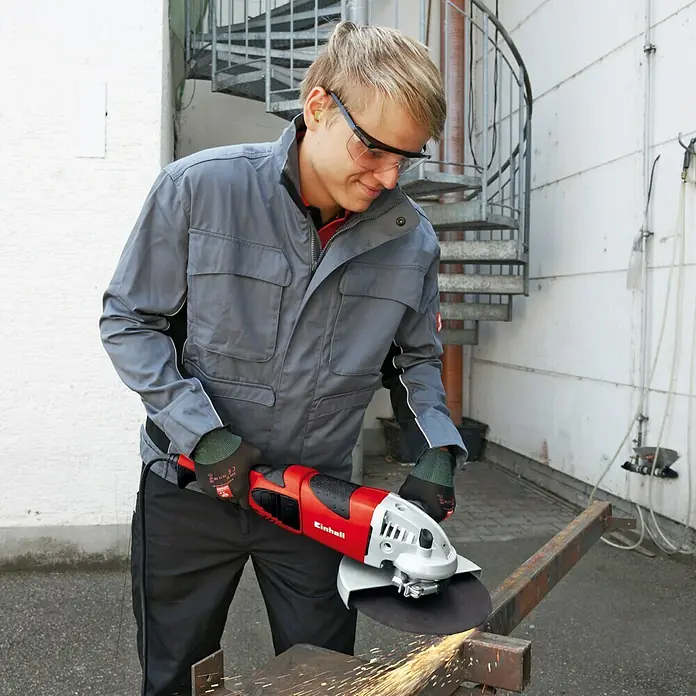 Einhell Expert Elektro-Winkelschleifer TE-AG 230/2000 - 2.000 W, 230 mm, Leerlaufdrehzahl: 6.500 U/min - Mann bei der Arbeit mit einem Einhell Winkelschleifer, Funken fliegen. Schutzbrille und Handschuhe sind Teil der Sicherheitsausrüstung.