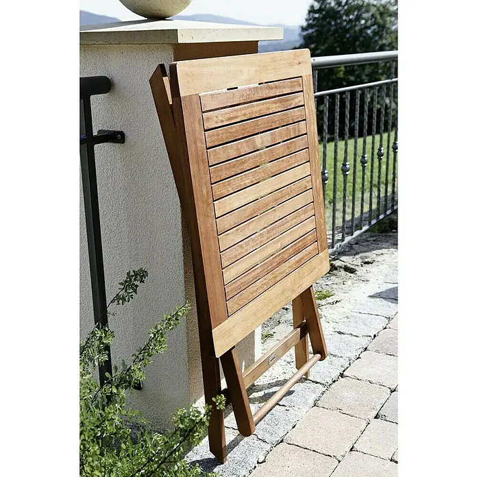 Sunfun Balkonmöbel-Set - 3 -tlg., Braun,Schwarz, Holz - Zusammengeklappter, rechteckiger Holztisch mit Lattenrost lehnt an einer Wand im Freien. Der Tisch ist aus hellem Holz gefertigt und für den Balkon geeignet.