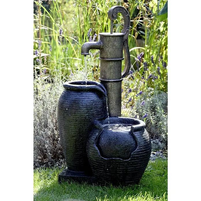 Dobar Kunststeinbrunnen - 47,5 x 38,5 x 84 cm - Dekorativer Gartenbrunnen mit Wasserpumpe und zwei dunklen Pflanzgefäßen, umgeben von üppigem Grün und lila Lavendel für eine entspannende Atmosphäre.