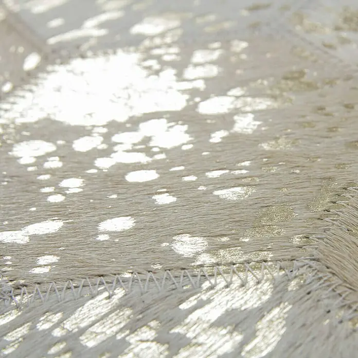Kayoom Lederteppich Dazzle 200 - Elfenbein/Gold, 170 x 120 cm, 100 % Leder - Nahaufnahme eines hellen Kuhfellteppichs mit goldenen Akzenten und dekorativer Ziernaht. Edles Design für ein stilvolles Ambiente.