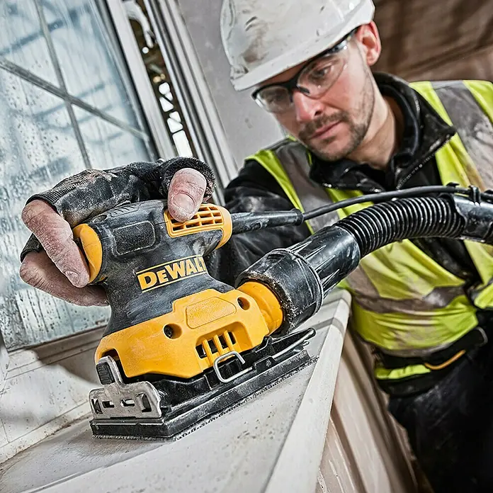 DeWalt Lijadora de banda eléctrica DWE6411 - 230 W, 14.000 r.p.m. - Un trabajador utiliza una lijadora orbital DeWalt en un marco de ventana. La herramienta es amarilla y negra, con sistema de extracción de polvo.
