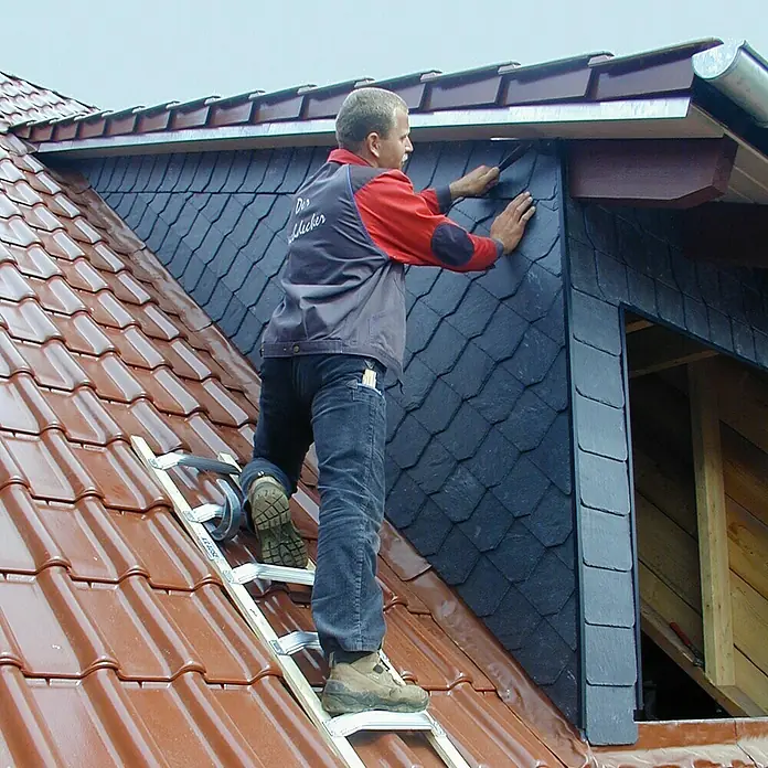 Krause Dachleiter - Länge: 5,05 m, Anzahl Tritte: 18 Stk., Aluminium, Holme aus wasserfestem, verleimtem, mehrlagigem Schichtholz - Dachdecker bei der Arbeit an einem Dachfenster mit Naturschiefer. Der Mann steht auf einer Dachleiter auf einem Ziegeldach.